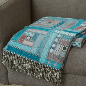 May include: A blue and pink patterned throw blanket with fringe on a grey sofa.