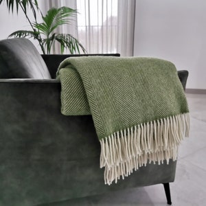 Può includere: Una coperta verde a spina di pesce con frange bianche, drappeggiata su una poltrona verde scuro.