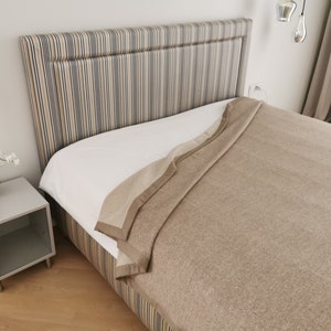 May include: A brown and beige blanket on a bed with a striped headboard. The bed is in a bedroom with a white nightstand and a small potted plant.