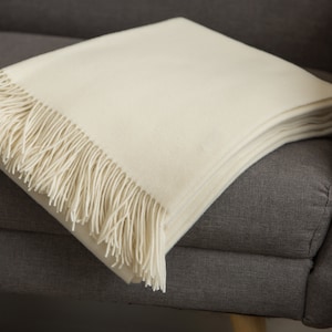 May include: A white throw blanket with a fringe border, folded and draped over a gray armchair.