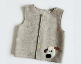May include: A sleeveless vest in a light beige herringbone pattern fabric. The vest features a round neckline, four light-colored snap buttons down the front, and a felt applique of a dog face with brown ears and a black nose on the lower front.
