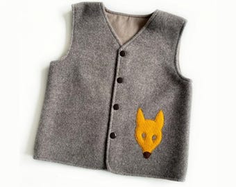 May include: A sleeveless grey vest featuring a V-neckline and four dark brown buttons down the front. The garment is made of a textured fabric and includes a yellow felt fox head appliqué on the lower right side with a small dark brown nose detail.