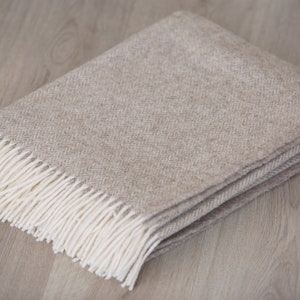 Pu&ograve; includere: Una coperta beige a spina di pesce con frange bianche.