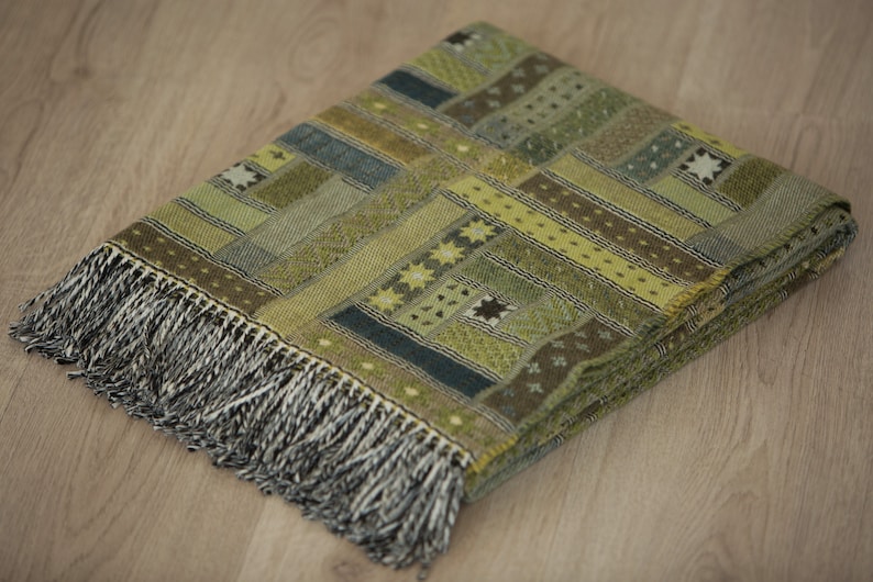 May include: A green and brown woven throw blanket with a geometric pattern and fringe trim.