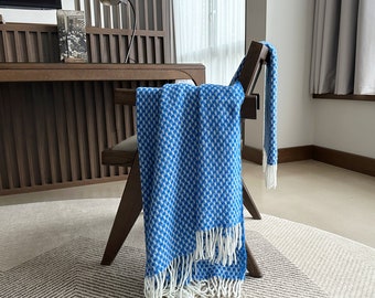May include: A blue and white patterned throw blanket draped over a wooden chair. The blanket has a fringe border and is made of a soft, woven fabric.