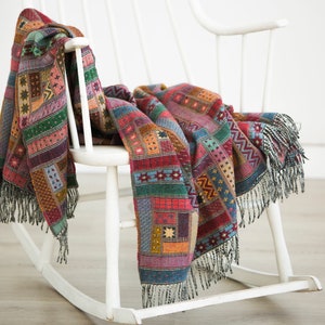 May include: A white rocking chair with a colourful patterned throw blanket draped over it. The blanket has a patchwork design with red, green, blue, and yellow colours.