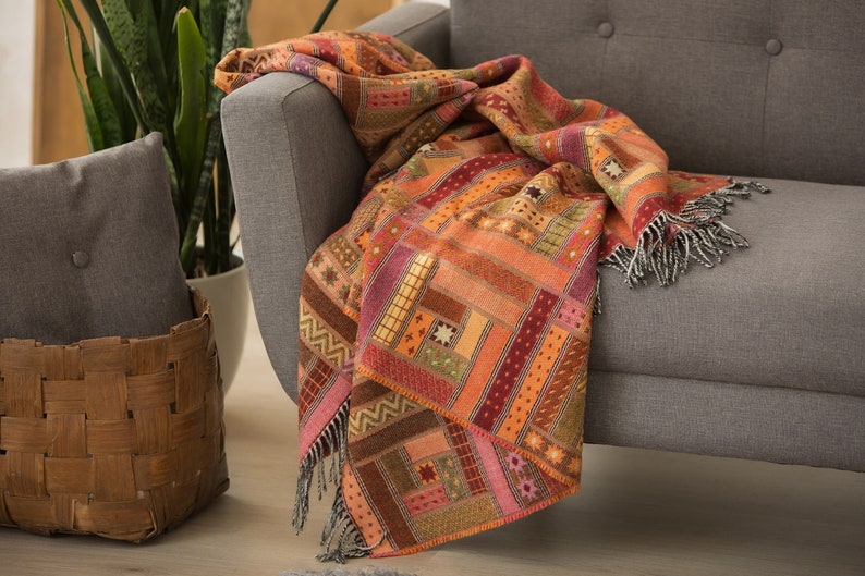 May include: A colourful throw blanket with a patchwork design in shades of orange, red, brown, and pink. The blanket is draped over a grey sofa.