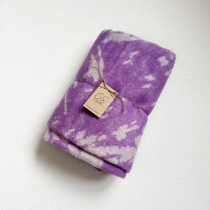 Peut inclure: Une couverture pliée en violet et blanc à motifs, attachée avec de la ficelle. Une petite étiquette brune avec le texte "GS" est attachée à la ficelle.