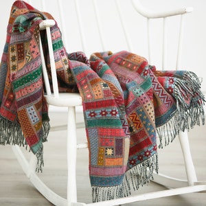 Peut inclure: Une couverture en laine tissée colorée avec des franges, drapé sur un fauteuil à bascule blanc.