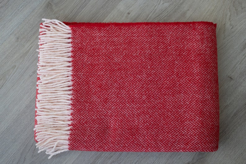 Pu&ograve; includere: Coperta in lana rossa e bianca a spina di pesce con frange.