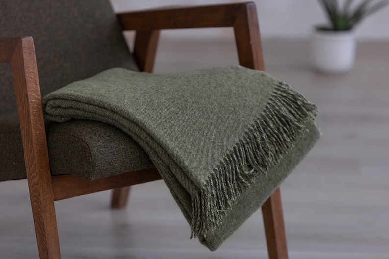 Puede incluir: Una manta de tiro verde con flecos en una silla de madera. La manta est&aacute; doblada y drapeada sobre la silla.