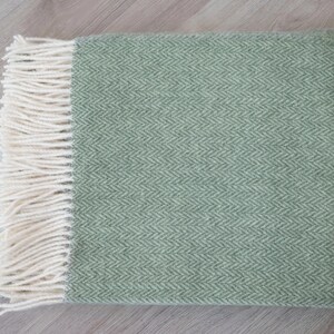 Pu&ograve; includere: Una morbida coperta verde con un motivo a spina di pesce e frange bianche.