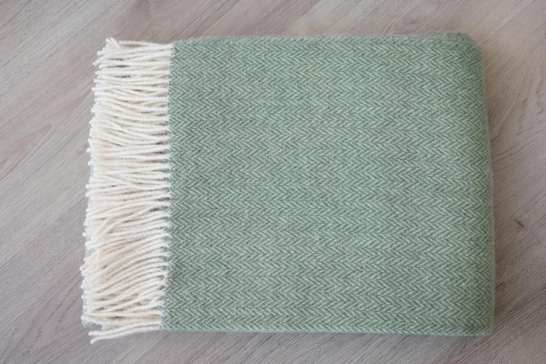 Pu&ograve; includere: Una morbida coperta verde con un motivo a spina di pesce e frange bianche.