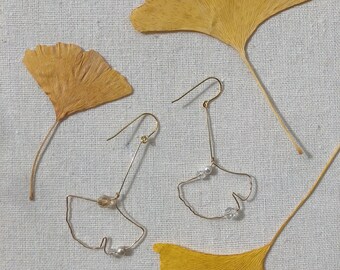May include: A pair of gold earrings shaped like ginkgo leaves with small pearl and crystal accents.