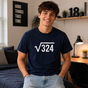 May include: A navy blue short-sleeved t-shirt featuring a white graphic print of the square root symbol followed by the number 324 centred on the chest. The garment has a classic crew neckline and a straight hemline, constructed from a solid fabric.