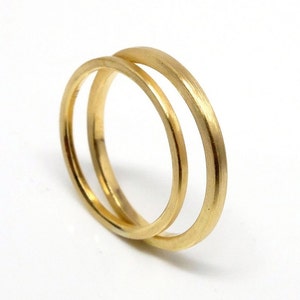 May include: Two gold wedding bands, one slightly larger than the other, are stacked together. The bands have a smooth, polished finish.