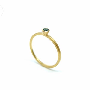 K&ouml;nnte beinhalten: Ein zarter Goldring mit einem kleinen, runden, blauen Edelstein in der Mitte.