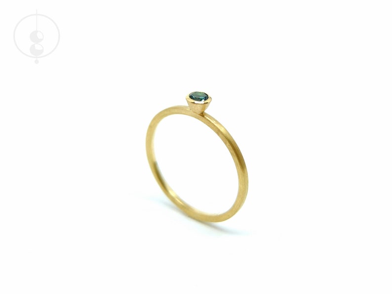 K&ouml;nnte beinhalten: Ein zarter Goldring mit einem kleinen, runden, blauen Edelstein in der Mitte.