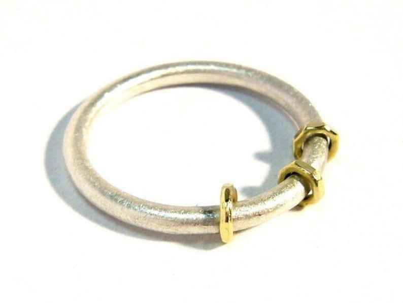 Silberring auf weißem Untergrund. Der Silberring ist von schräg oben fotografiert und hat eine matte Oberfläche. Die Ringschiene ist aus 2mm dickem Runddraht angefertigt und der Ring mit drei verschieden facettierte Goldösen verziert.