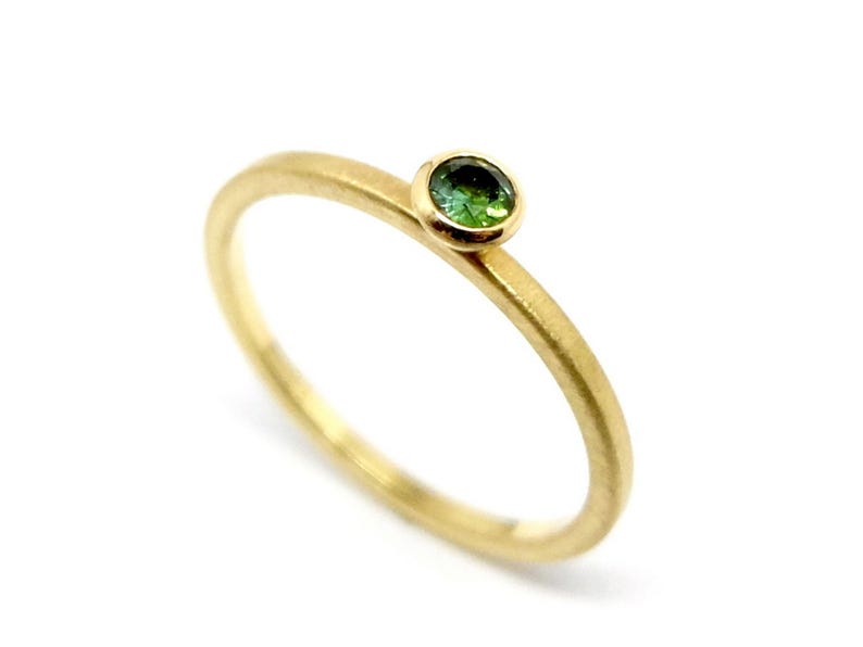 K&ouml;nnte beinhalten: Ein schlichter Goldring mit einem kleinen gr&uuml;nen Edelstein in der Mitte.