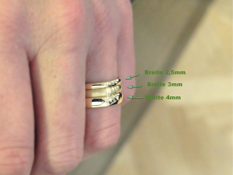 Nahaufnahme von Hand, an deren Ringfinger 3 verschieden breite Goldringe stecken. Der schmalste Ring ist 2,5mm breit, der mittlere 3mm breit und der breiteste 4mm. 2 Ringe glänzen, ein Ring hat eine matte Oberfläche.