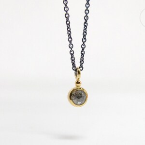 Puede incluir: Un delicado collar de cadena de plata con un colgante de oro con un diamante gris redondo.