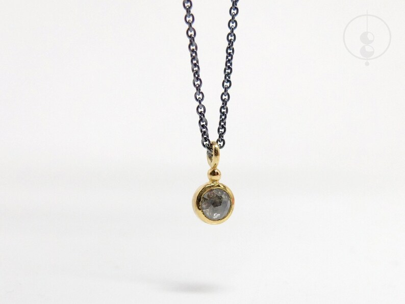 Puede incluir: Un delicado collar de cadena de plata con un colgante de oro con un diamante gris redondo.
