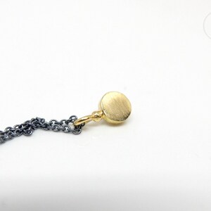 Puede incluir: Un collar de cadena de oro con un peque&ntilde;o colgante redondo de oro. La cadena est&aacute; hecha de dos metales diferentes, uno negro y otro plateado.