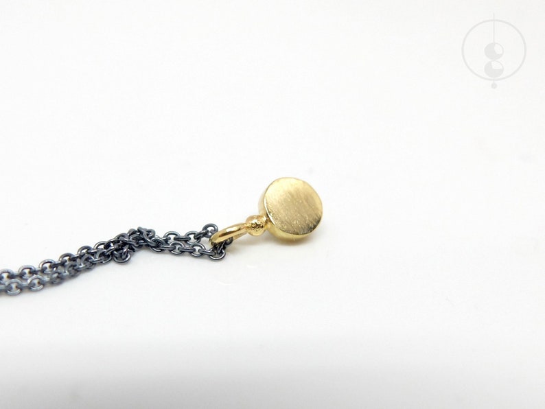 Puede incluir: Un collar de cadena de oro con un peque&ntilde;o colgante redondo de oro. La cadena est&aacute; hecha de dos metales diferentes, uno negro y otro plateado.