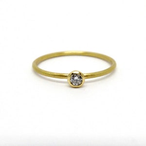 Nahaufnahme von einem schmalen Gelbgoldring auf weißem Hintergrund. Der Ring hat eine schlichte, runde Ringschiene und eine Zargenfassung mit einem weißen Diamanten. Der Goldring liegt mit der Fassung nach vorne.