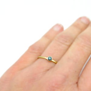 K&ouml;nnte beinhalten: Ein zarter Goldring mit einem kleinen, runden, blauen Edelstein.