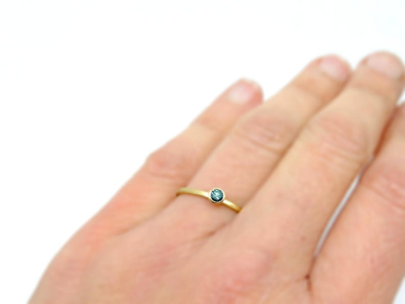 K&ouml;nnte beinhalten: Ein zarter Goldring mit einem kleinen, runden, blauen Edelstein.