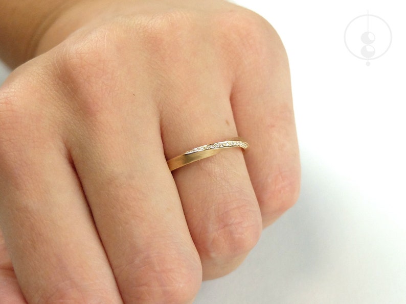 Nahaufnahme von einem Möbius-Ring aus Roségold, der auf dem Ringfinger einer Hand sitzt. Auf der oberen Kante der Drehung sind viele kleine Diamanten pavee gefasst.
