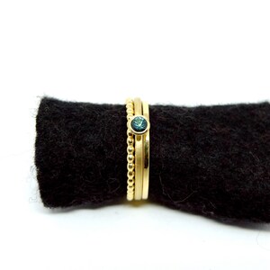 K&ouml;nnte beinhalten: Drei goldene Ringe, die &uuml;bereinander gestapelt sind. Der oberste Ring hat einen kleinen, runden, blauen Edelstein.