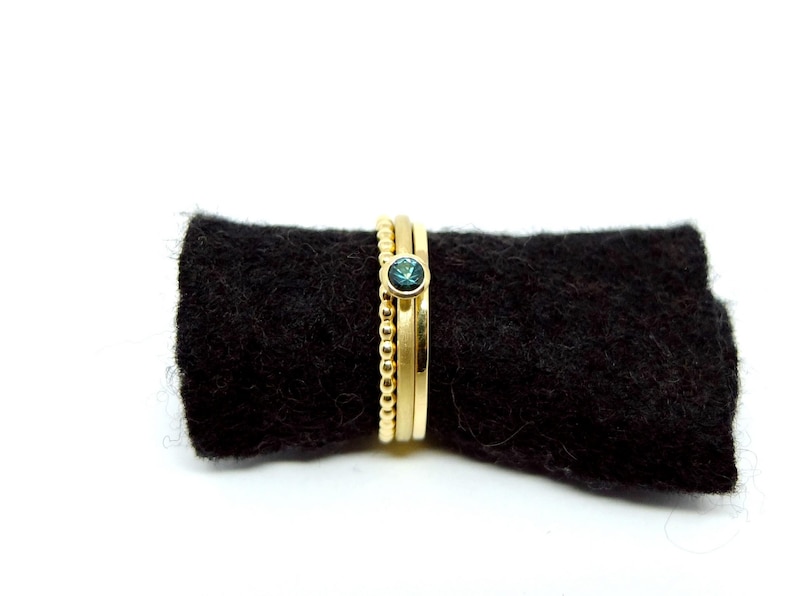 K&ouml;nnte beinhalten: Drei goldene Ringe, die &uuml;bereinander gestapelt sind. Der oberste Ring hat einen kleinen, runden, blauen Edelstein.