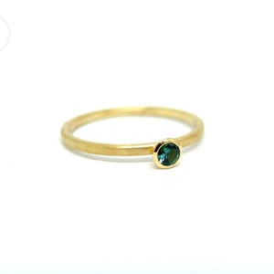 K&ouml;nnte beinhalten: Ein schlichter Goldring mit einem kleinen, runden, dunkelgr&uuml;nen Edelstein.