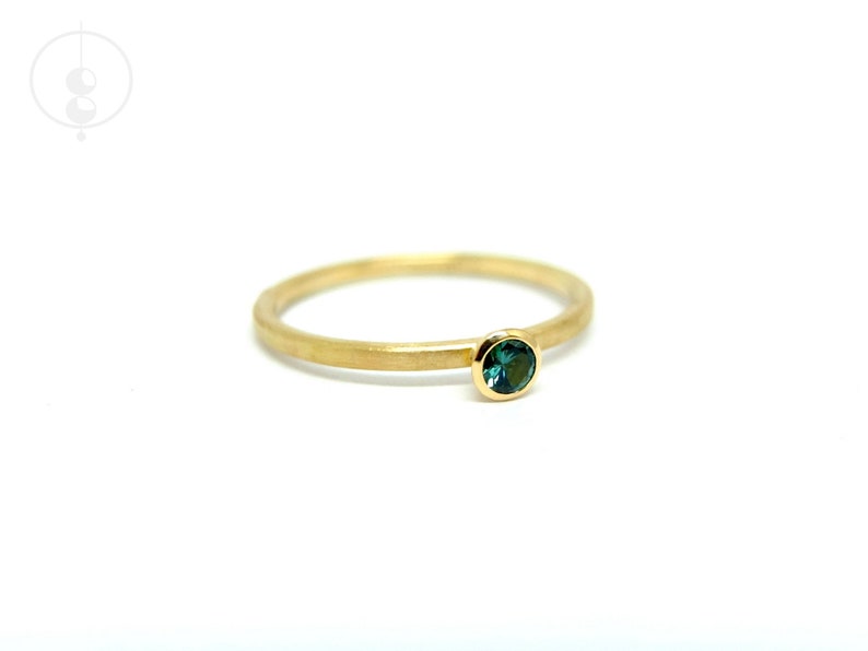 K&ouml;nnte beinhalten: Ein schlichter Goldring mit einem kleinen, runden, dunkelgr&uuml;nen Edelstein.