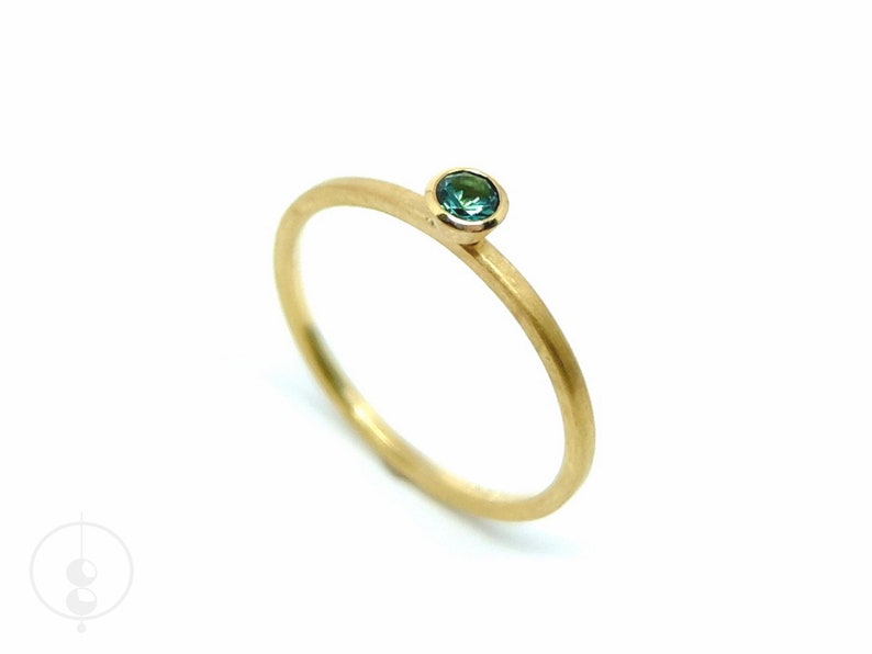 K&ouml;nnte beinhalten: Ein schlichter Goldring mit einem kleinen, runden, blaugr&uuml;nen Edelstein in der Mitte.