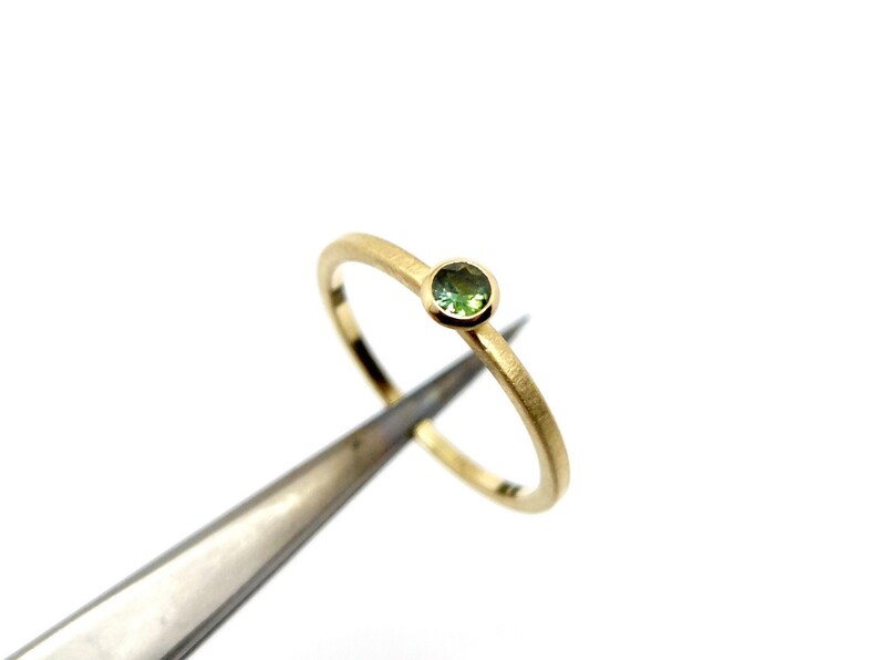 K&ouml;nnte beinhalten: Ein zarter Goldring mit einem kleinen, runden gr&uuml;nen Edelstein.