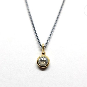 Puede incluir: Un collar de cadena de plata con un colgante de oro con un diamante redondo y transparente.
