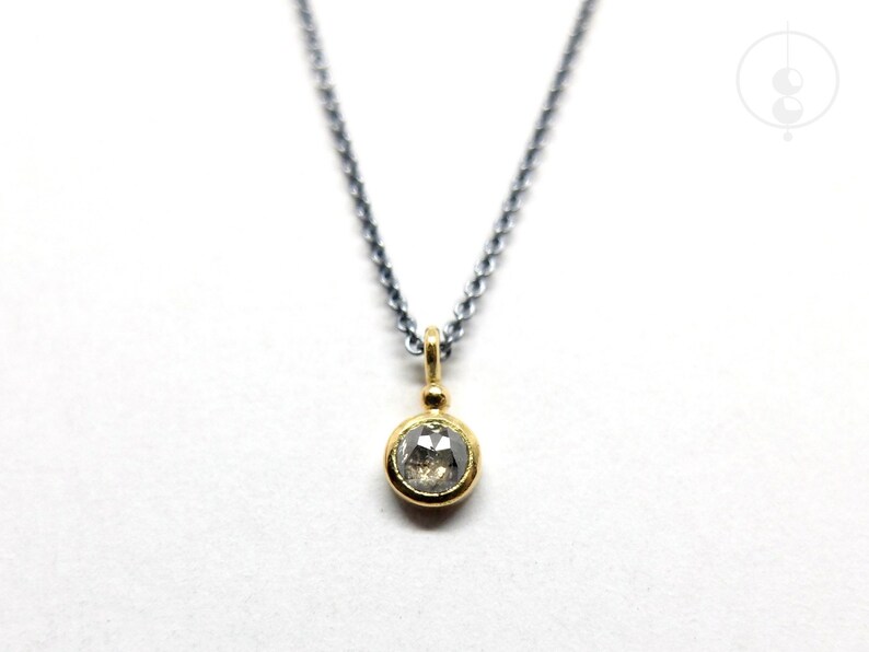 Puede incluir: Un collar de cadena de plata con un colgante de oro con un diamante redondo y transparente.