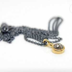 Puede incluir: Un collar de cadena de plata con un colgante de oro con un diamante gris redondo.