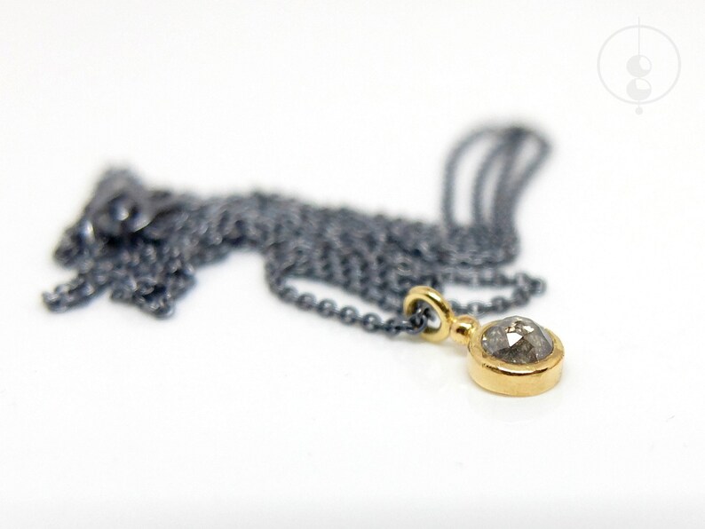 Puede incluir: Un collar de cadena de plata con un colgante de oro con un diamante gris redondo.