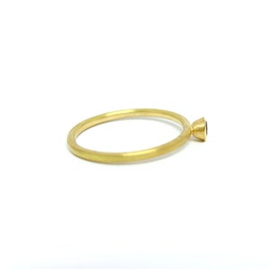 K&ouml;nnte beinhalten: Ein schlichter Goldring mit einem kleinen schwarzen Edelstein in einer Zargenfassung.