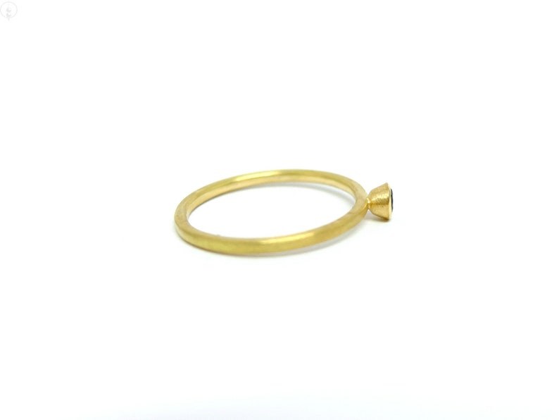 K&ouml;nnte beinhalten: Ein schlichter Goldring mit einem kleinen schwarzen Edelstein in einer Zargenfassung.