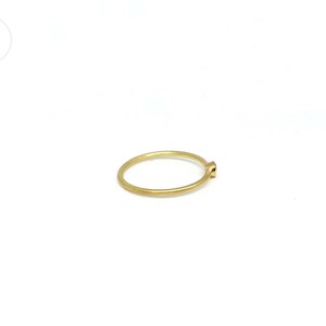 May include: A thin, circular gold ring with a matte, brushed texture. The band is uniform in thickness and features a single, small, round, bezel-set stone at the top. The metal has a warm, yellow hue and a subtle, non-reflective finish.