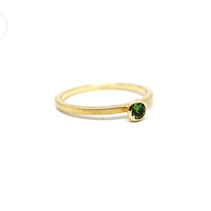 K&ouml;nnte beinhalten: Ein schlichter Goldring mit einem kleinen gr&uuml;nen Edelstein.