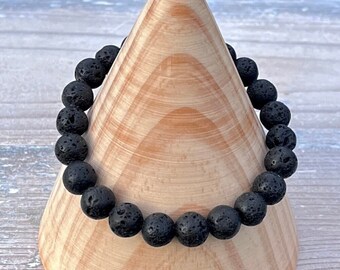 May include: A black lava rock beaded bracelet on a wooden display stand.