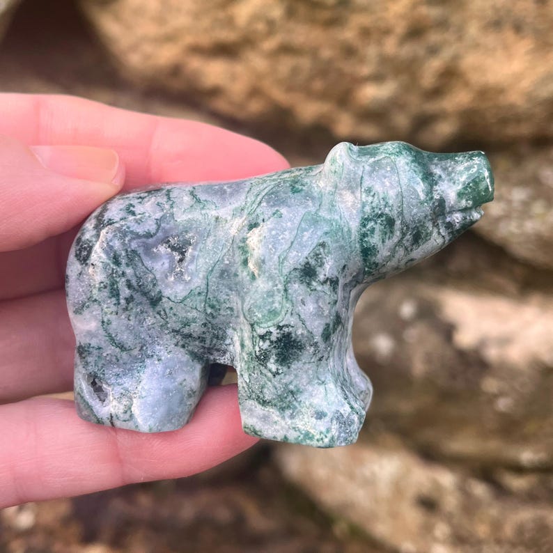 Puede incluir: Una peque&ntilde;a figura de oso tallada a mano en piedra de &aacute;gata musgosa. La escultura presenta una superficie pulida con un patr&oacute;n jaspeado de verde bosque profundo, blanco transl&uacute;cido e inclusiones grises en toda la forma del oso.