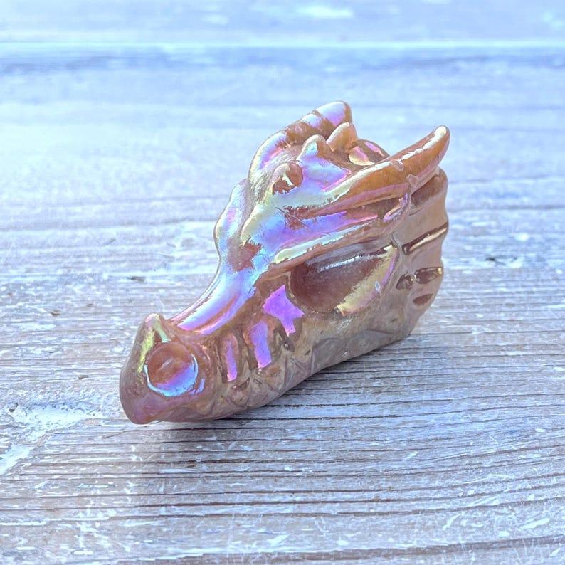 K&ouml;nnte beinhalten: Eine geschnitzte Drachenkopf-Figur mit schillerndem Finish. Die Skulptur hat eine braune Grundfarbe mit schimmernden Farbt&ouml;nen von Lila, Blau und Gold. Zu den Merkmalen des Drachen geh&ouml;ren H&ouml;rner, eine Schnauze und detaillierte Schuppen.